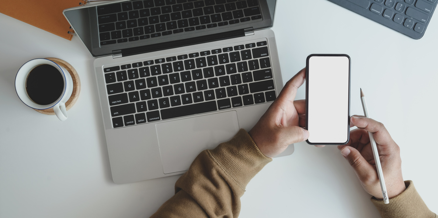Faceless man with mobile phone at desk with laptop